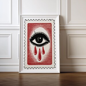 Pode incluir: Impressão de arte emoldurada com um olho estilizado com cílios pretos e uma lágrima caindo do olho. O olho está sobre um fundo vermelho com uma borda de selo postal. A obra de arte é exibida em uma moldura branca.