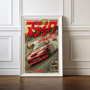 Puede incluir: Póster enmarcado con un coche deportivo rojo derrapando en una pista, con texto y gráficos japoneses. El póster tiene una estética vintage, con un marco blanco y un suelo de madera.