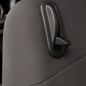 May include: Close-up of a gray car seat with a black plastic lever. The seat has a textured fabric and is partially visible, with the steering wheel in the background. Automotive interior detail.