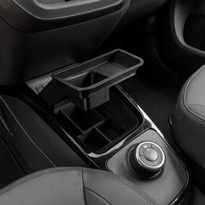 Puede incluir: Un organizador de consola de coche negro con una bandeja y múltiples compartimentos. El organizador está diseñado para encajar en el área de la consola central de un vehículo. La imagen muestra una vista de cerca del organizador, destacando sus características y diseño.