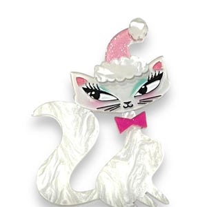 Peut inclure: Broche en forme de chat ornée d'un bonnet de Père Noël. La broche présente un corps blanc à effet marbré, un nœud papillon rose et un bonnet de Père Noël rose et blanc pailleté. Le chat a des cils noirs et un fard à paupières turquoise.