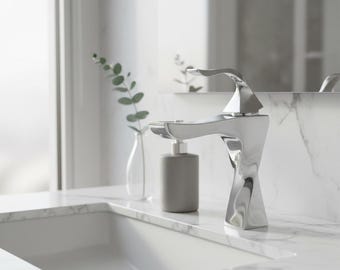 Puede incluir: Un moderno grifo cromado con un diseño único y retorcido. El grifo está sobre una encimera de mármol blanco, con un dispensador de jabón gris y un pequeño jarrón con vegetación. La estética general es limpia y contemporánea.
