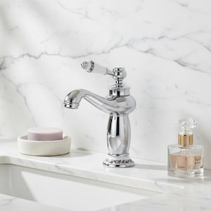 May include: A shiny chrome tap with a white handle and ornate detailing. A lavender soap bar rests in a small, off-white dish. A clear perfume bottle with a gold cap and crystal stopper is also present, suggesting a bathroom or vanity setting.
