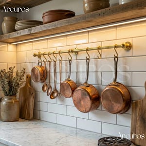 May include: A kitchen scene featuring copper pots and utensils hanging from a brass rail against white tiled walls. A wooden shelf above holds plates and bowls. A marble countertop and cutting boards complete the rustic aesthetic.
