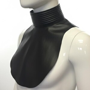 May include: A black, high-collared neck piece with a layered design at the neck and a smooth, draped front. The neck piece is displayed on a white mannequin.