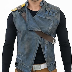 Puede incluir: Un chaleco azul y marrón con apariencia de cuero. El chaleco tiene una correa marrón en el pecho y un acento amarillo en el hombro. La persona lleva una camisa negra de manga larga y un cinturón blanco.