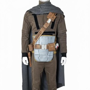 May include: A brown and gray costume with a cape, designed to resemble a character from a science fiction film. The costume includes a long-sleeved shirt, pants, a belt with pouches, and a chest plate. A gray scarf is draped around the neck.