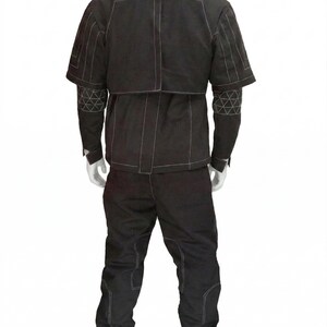 K&ouml;nnte beinhalten: Schwarzes zweiteiliges Outfit mit wei&szlig;en Steppn&auml;hten. Die Jacke hat einen hohen Kragen und kurze &Auml;rmel mit geometrischen Mustern auf den &Auml;rmeln. Die Hose hat verst&auml;rkte Knie. Das Outfit wird auf einer Schaufensterpuppe pr&auml;sentiert.