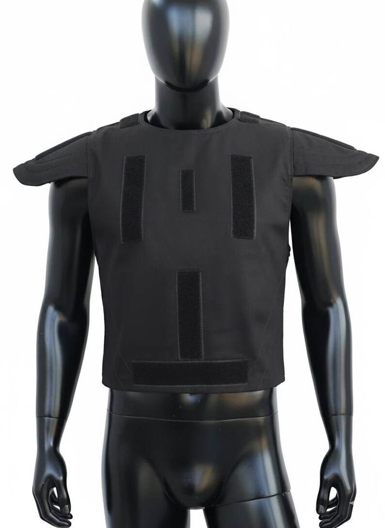 May include: Black tactical vest with shoulder pads and multiple Velcro panels. The vest is displayed on a black mannequin. This protective gear is designed for security and law enforcement.