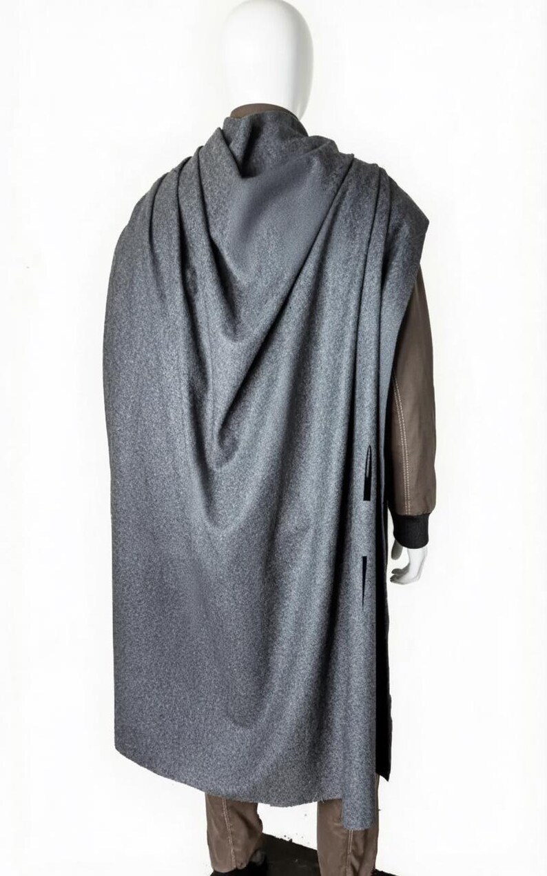 May include: A gray cape with a textured pattern, draped over a mannequin. The cape has a long, flowing design and features vertical slits on the side. The mannequin is wearing a brown jacket underneath.