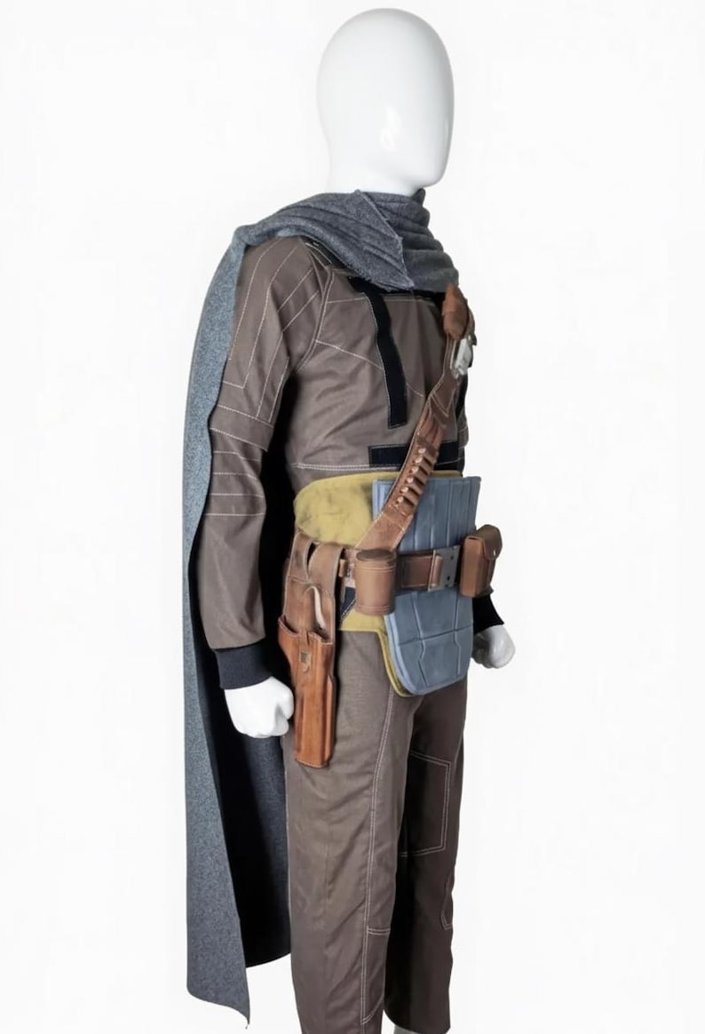 May include: A brown and gray costume with a cape, designed to resemble a character from a science fiction film. The outfit includes a long-sleeved top, pants, and a utility belt with pouches and a holster. A gray scarf and cape complete the ensemble.