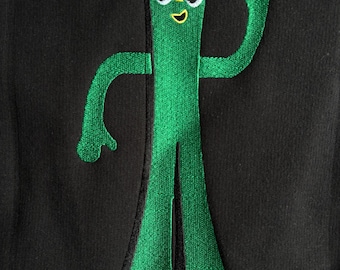 May include: Black sweatshirt featuring a green embroidered Gumby character. The character has a smiling face, yellow head, and is waving. The design is centered on the front of the sweatshirt.