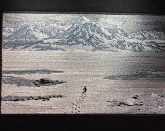 May include: Embroidered patch featuring a mountain landscape with a figure walking across a snowy expanse. The design uses shades of gray and blue, with detailed stitching creating texture and depth. The patch is rectangular.
