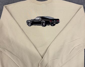 May include: A beige sweatshirt featuring an embroidered black classic car design. The car has detailed silver wheels and red taillights. The sweatshirt has a crew neck and long sleeves, perfect for casual wear.