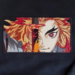 May include: A black sweatshirt featuring a rectangular embroidered patch on the chest. The embroidery depicts an anime character with spiky red and yellow hair, intense red eyes, and a sword with a flame-patterned blade held vertically.