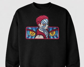 May include: Black sweatshirt featuring an embroidered anime character with red hair and blue and white facial markings. The character is set against a rectangular patch with blue and red stripes and Japanese text.
