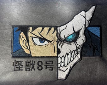 May include: Embroidered patch featuring a split design: one half depicts a human face with a determined expression, the other a white skull with a glowing blue eye. The Japanese text "Kaiju No. 8" is below the image.