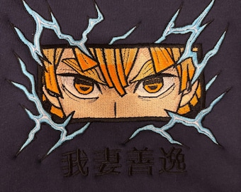 May include: Navy blue hoodie featuring an embroidered design of anime eyes with orange and yellow hair, surrounded by blue lightning bolts. The design includes Japanese characters below the eyes.