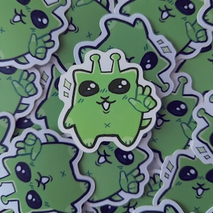 以下が含まれることがあります： 漫画の宇宙人キャラクターが描かれた緑色のステッカーのコレクション。宇宙人は大きな黒い目を持ち、笑顔の口をしており、ピースサインをしています。ステッカーは白い背景にあります。