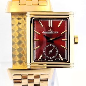 Peut inclure: Une montre-bracelet dorée avec un cadran rectangulaire et un bracelet assorti. Le cadran est rouge foncé avec des aiguilles et des marqueurs dorés, et un petit cadran secondaire. La montre est marquée "JAEGER-LECOULTRE" et "SWISS MADE".