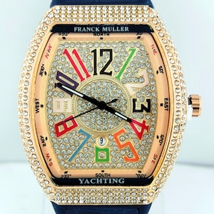 Puede incluir: Un reloj de pulsera de lujo con caja dorada y correa de cuero azul. La esfera del reloj presenta un diseño con diamantes y números coloridos, con el texto "FRANCK MULLER NORTH SOUTH YACHTING". El reloj tiene una corona de oro rosa.