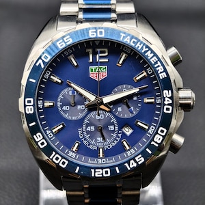 May include: A TAG Heuer Formula 1 chronograph watch with a blue dial and a stainless steel bracelet featuring blue center links. The watch includes a tachymeter bezel, three sub-dials, a date window at the four o'clock position, and luminous hands.