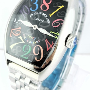 Puede incluir: Un reloj Franck Muller Crazy Color Dreams de acero inoxidable. La esfera negra presenta números arábigos coloridos y las palabras "Franck Muller Geneve" y "Crazy Color Dreams". El reloj tiene un brazalete plateado y una corona con una gema azul.