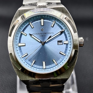 Könnte beinhalten: Eine silberfarbene Armbanduhr aus Edelstahl mit einem hellblauen Zifferblatt im Sonnenschliff, silbernen Indizes und Zeigern. Das Zifferblatt zeigt den Schriftzug Vacheron Constantin Geneve, ein Datumsfenster bei drei Uhr und Swiss Made unten.