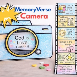 Op de afbeelding: Een lichtblauwe en witte Memory Verse Camera met de tekst "God is Liefde. I Johannes 4:8" in de lens. Een filmstrip met bijbelverzen staat rechts. Het woord "Camera" is rood.