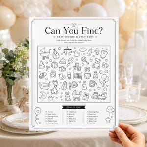 Może przedstawiać: Biała papierowa gra typu szukaj i znajdź na baby shower z czarnymi rysunkami liniowymi artykułów dziecięcych. Nagłówek brzmi Can You Find? Baby Shower Search Game. Poniżej znajduje się siatka ikon, w tym wózek, grzechotka, miś i klocki, z listą 18 przedmiotów do znalezienia na dole.