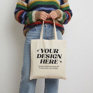 May include: A cream-colored canvas tote bag featuring the black printed text "YOUR DESIGN HERE" in a bold serif font, accented by four-pointed star icons, with smaller text below reading "Instant digital mockup file to showcase your design."