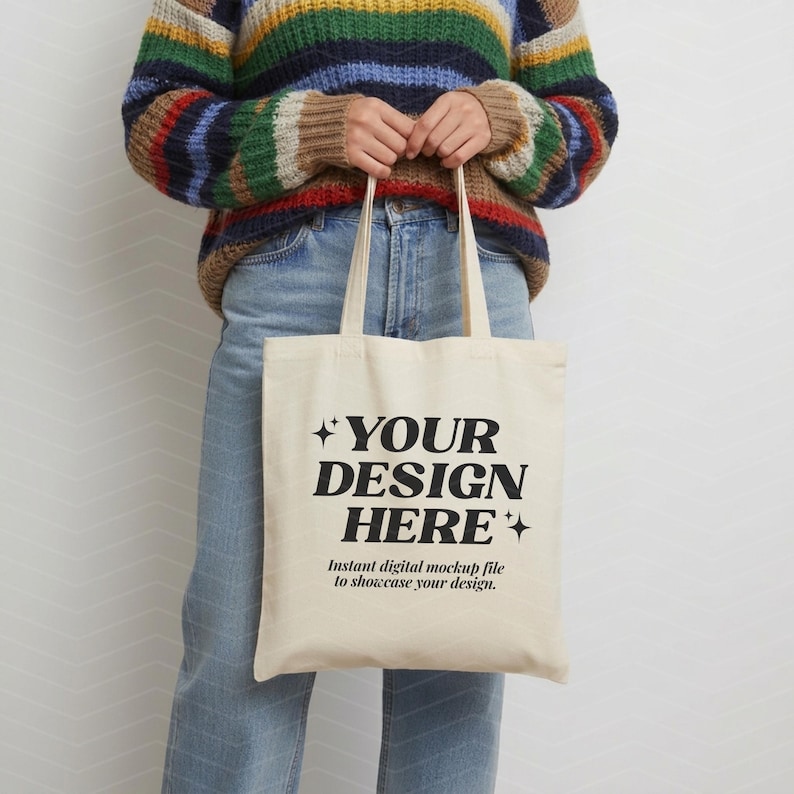 May include: A cream-colored canvas tote bag featuring the black printed text "YOUR DESIGN HERE" in a bold serif font, accented by four-pointed star icons, with smaller text below reading "Instant digital mockup file to showcase your design."