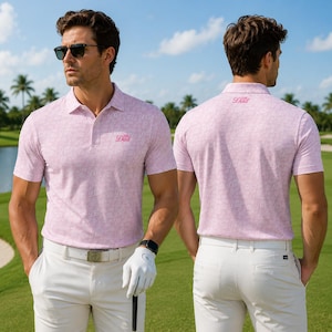 May include: A light pink polo shirt with a repeating pattern and the word "Dad" in pink. The shirt is paired with white pants and a white belt. The person is wearing sunglasses and a golf glove.