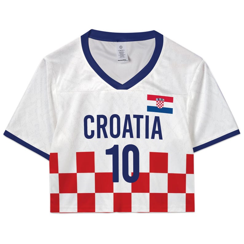 May include: White crop top jersey with blue trim and a V-neck. The front features the word "CROATIA" in navy blue, the number "10", and the Croatian flag. The bottom hem has a red and white checkered pattern.