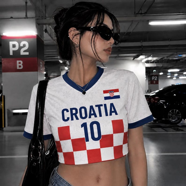 May include: White and blue Croatia soccer jersey with the word "CROATIA" and the number "10" printed on the front. The jersey has a red and white checkered pattern at the bottom. The Croatian flag is on the right chest.