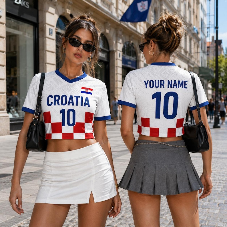 May include: Two women wearing white Croatia soccer jerseys with blue trim, the word "CROATIA" and the number "10" in blue. The jerseys have a red and white checkered pattern at the bottom. One woman wears a white skirt, the other a gray pleated skirt.