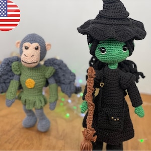 May include: Two handmade crochet dolls: a green-skinned witch in a black dress and hat, holding a broom, and a monkey with wings, wearing a green outfit. The dolls are set against a neutral background, showcasing their detailed craftsmanship.