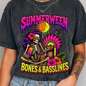 May include: A charcoal grey acid-wash t-shirt featuring a graphic print of a skeleton with purple hair, holding a popsicle, sitting next to a jukebox. The text reads SUMMERWEEN BONES & BASSLINES in bright pink and yellow with a melting effect.