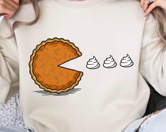 Puede incluir: Sudadera beige con un gráfico humorístico de un pastel al estilo Pac-Man, comiendo tres formas de remolino blanco. La imagen incluye el texto "300 DPI HIGH QUALITY PNG FILE" en la parte inferior en una pancarta roja.