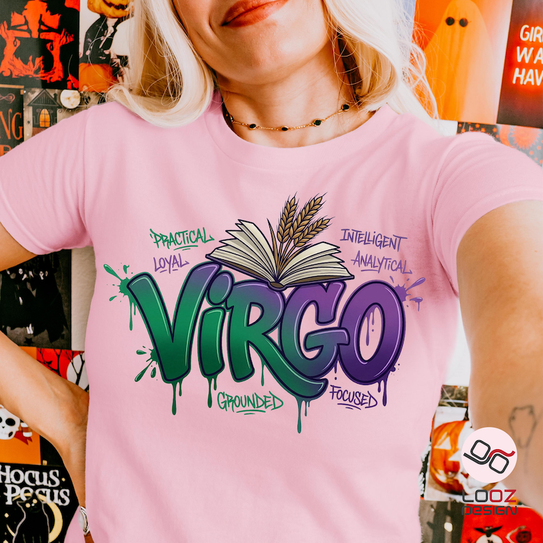 May include: A light pink t-shirt featuring a green and purple graphic of the word "Virgo" with a book and wheat design. The shirt also includes the words "Practical, Loyal, Grounded, Focused, Intelligent, and Analytical."