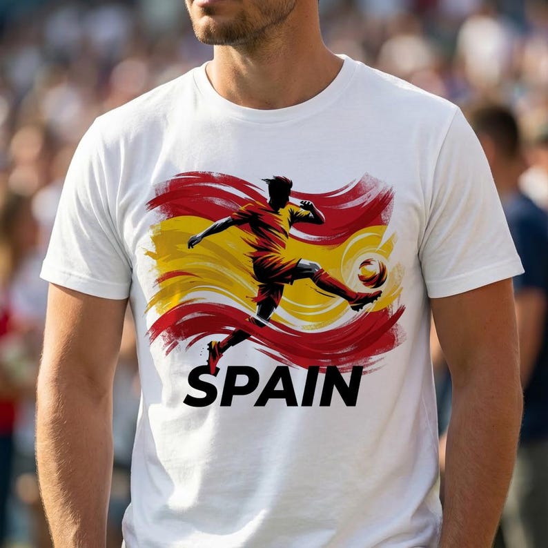 Puede incluir: Camiseta blanca con un jugador de f&uacute;tbol pateando un bal&oacute;n, sobre un fondo de pinceladas rojas, amarillas y naranjas. La palabra "SPAIN" est&aacute; impresa en negrita negra debajo. Prenda de vestir informal.