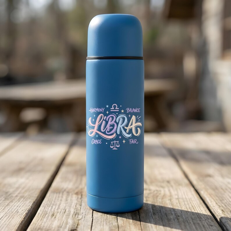 May include: A blue insulated water bottle with a black cap. The bottle features the word "Libra" in a colorful script, along with the words "Harmony, Balance, Grace, Fair" and a Libra symbol.