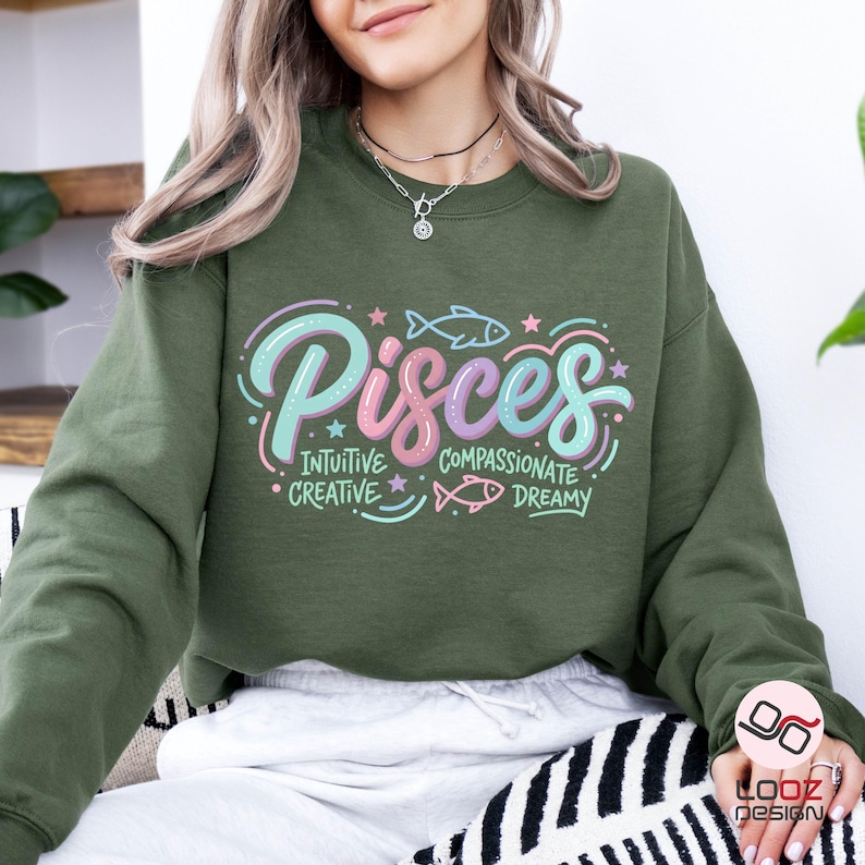 May include: Olive green sweatshirt with the word "Pisces" in a pastel color scheme. The design includes fish illustrations and the words "Intuitive, Creative, Compassionate, Dreamy". A casual, comfortable top.