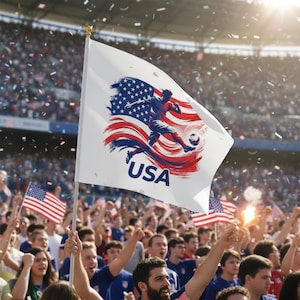 May include: A white flag with a USA soccer design featuring a player kicking a soccer ball, with the American flag in the background. The flag is held up by a crowd of people in a stadium, with confetti falling from above.