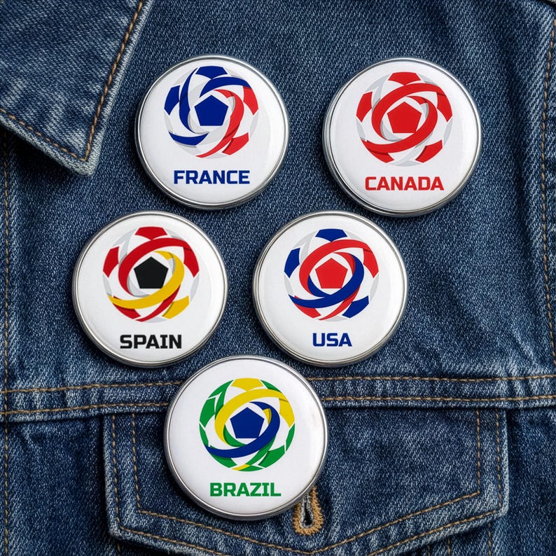 May include: Five round, white pinback buttons with colorful soccer ball designs and country names: France, Canada, Spain, USA, and Brazil. The buttons are on a blue denim jacket.