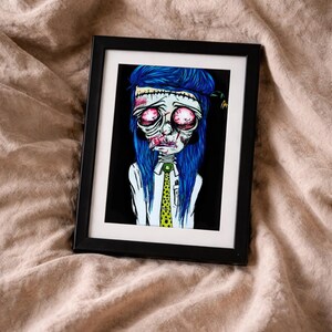 May include: A framed art print featuring a stylized illustration of a character with vibrant blue hair, large red eyes, and visible stitches on the forehead. The character wears a white collared shirt and a bright yellow tie with black polka dots.