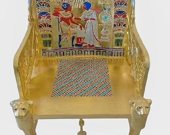 May include: A gold-colored throne with intricate carvings and colorful inlays. The back of the chair features a detailed scene with figures, and the legs are designed with lion heads and paws. The seat has a patterned design.