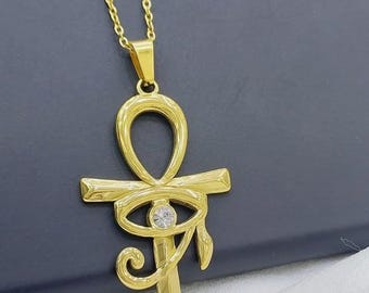 Op de afbeelding: Goudkleurige ankh-hangerketting met een fijne ketting. De ankh heeft een oogontwerp met een kleine, heldere edelsteen in het midden. De hanger is ongeveer 3,8 cm lang.