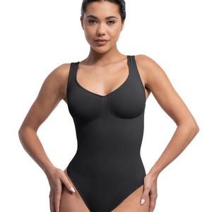 Puede incluir: Un body negro con escote en forma de pico y tirantes anchos. La prenda de una pieza tiene una silueta ajustada y está diseñada para alisar y dar forma al cuerpo. La tela parece ser un material liso y mate.