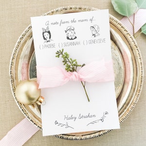 May include: A white card with a handwritten note that says "A note from the mom of..." with three illustrations of girls with names below each illustration: Phoebe, Susannah, and Genevieve. The card is signed "Haley Strahan" with a decorative flourish.